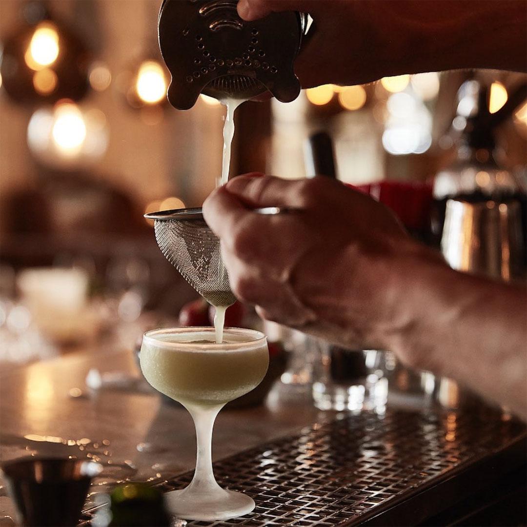 En person häller upp en drink i ett cocktailglas.