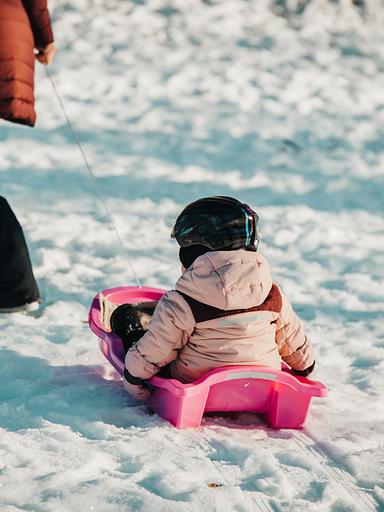 Ett barn åker i en rosa pulka.