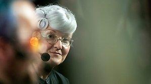 kvinna med fin håruppsättning och mikrofon tittar rakt mot betraktaren