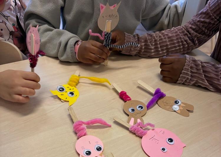 Barnhänder som håller i pappfigurer skapade på glasspinne.