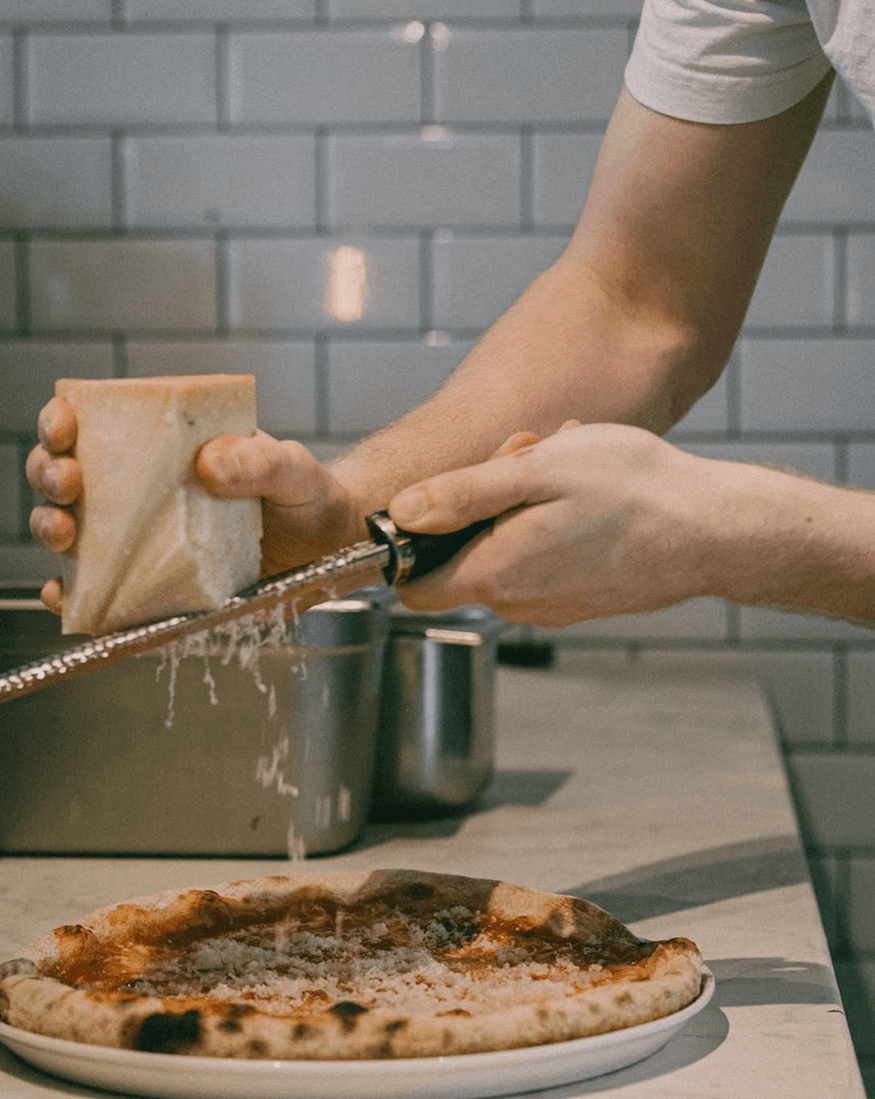 En man river ost på en pizza.