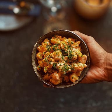 En hand håller en skål med popcorn prawns.