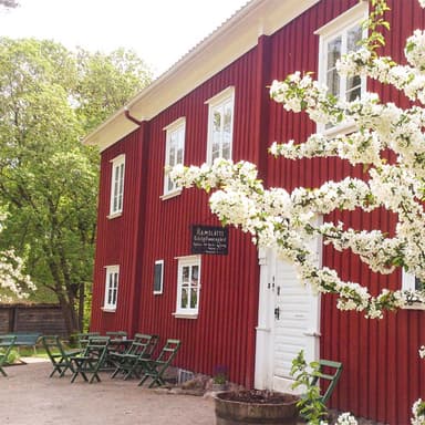 En röd träbyggnad omgiven av lummig skog.