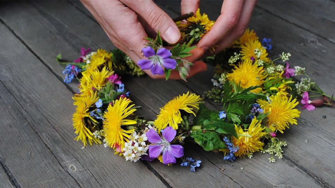 En person binder en krans med gula och lila blommor.