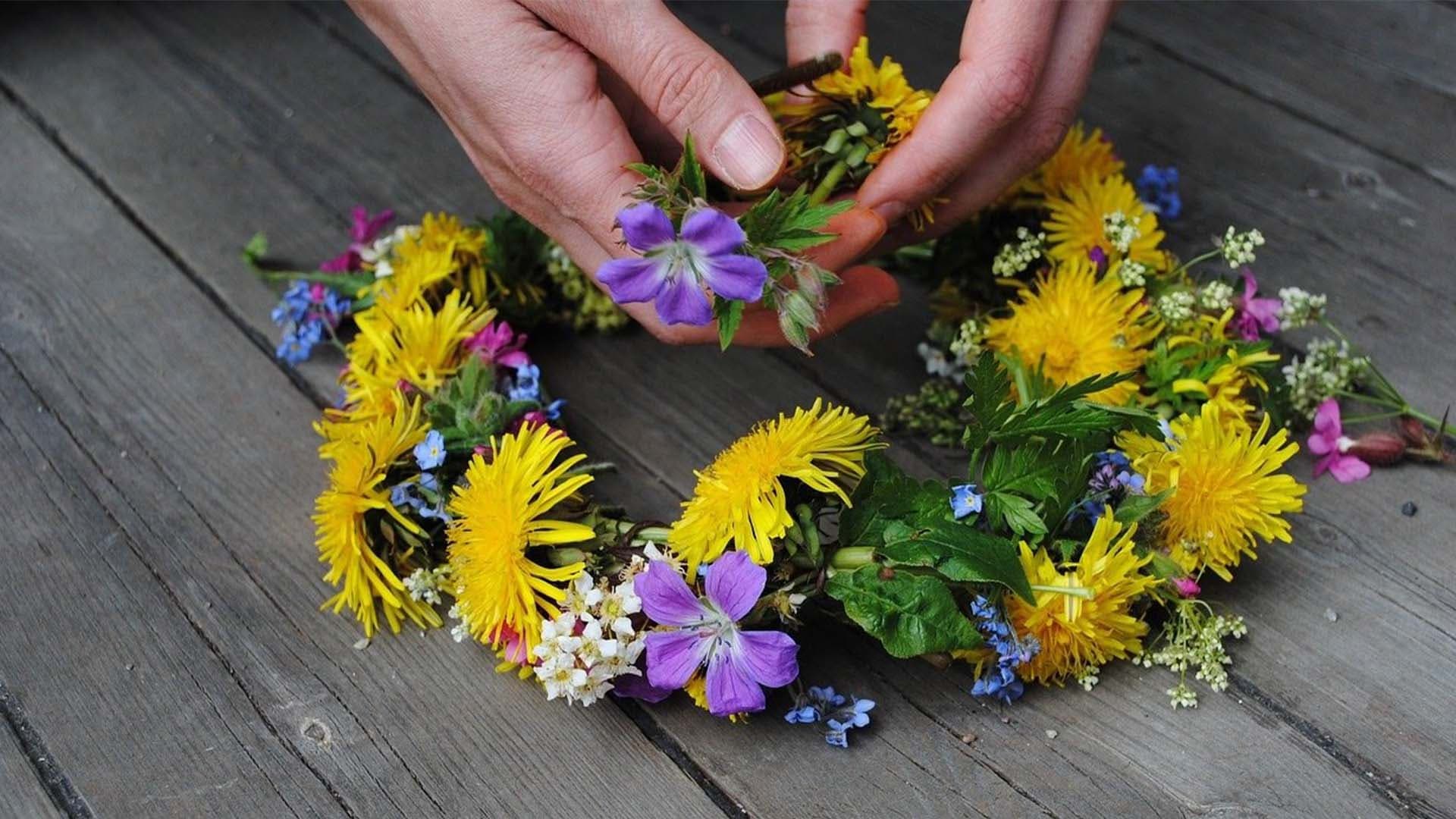 En person binder en krans med gula och lila blommor.