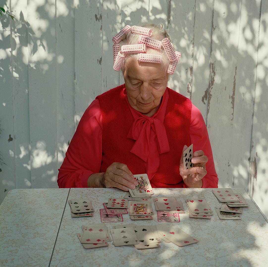 dam med papiljotter och röd stickad tröja spelar kort