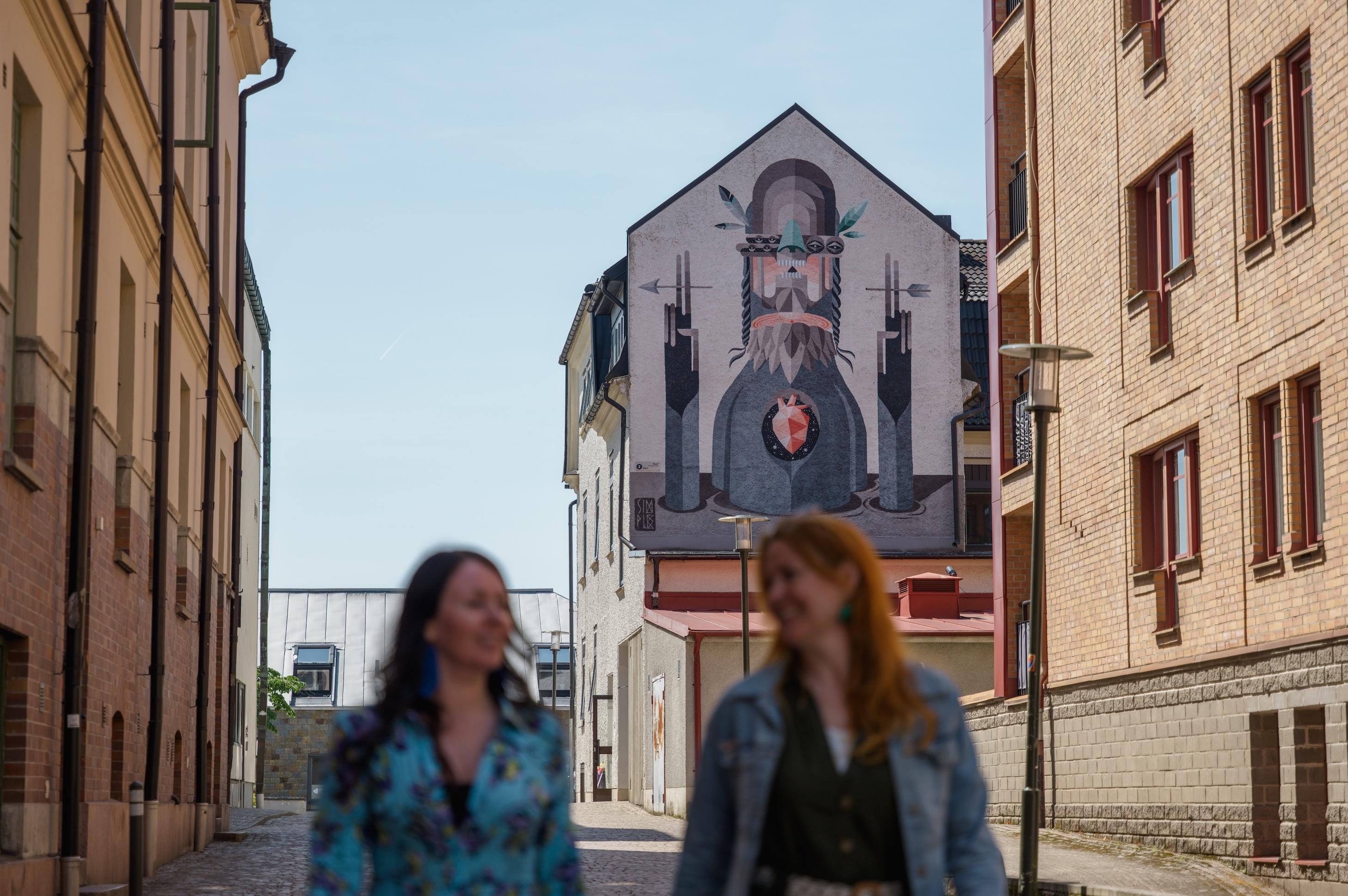 Två kvinnor går tillsammans framför en muralmålning.