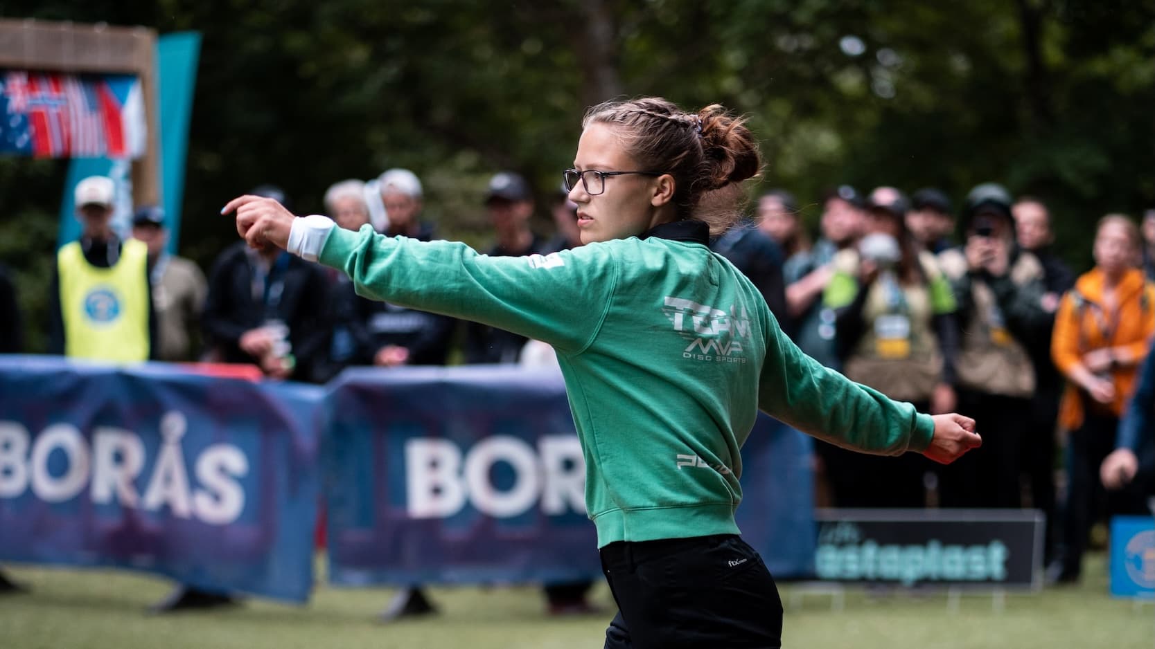 En tjej spelar disc golf med publik bakom.