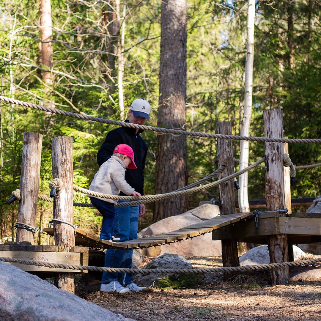 Pappa och dotter går över liten träbro utomhus på en inte nudda marken-park